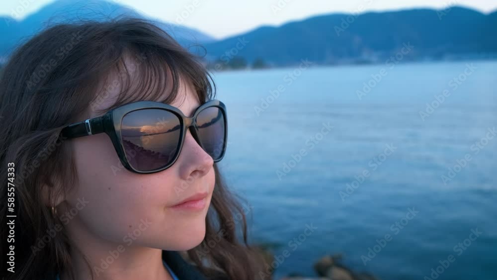 One child relax by sea with mountains. A happy little girl in glasses relax on shore against blue clear sea by mountains. One child relax by sea with mountains. A happy little girl in glasses relax on shore against blue clear sea by mountains.