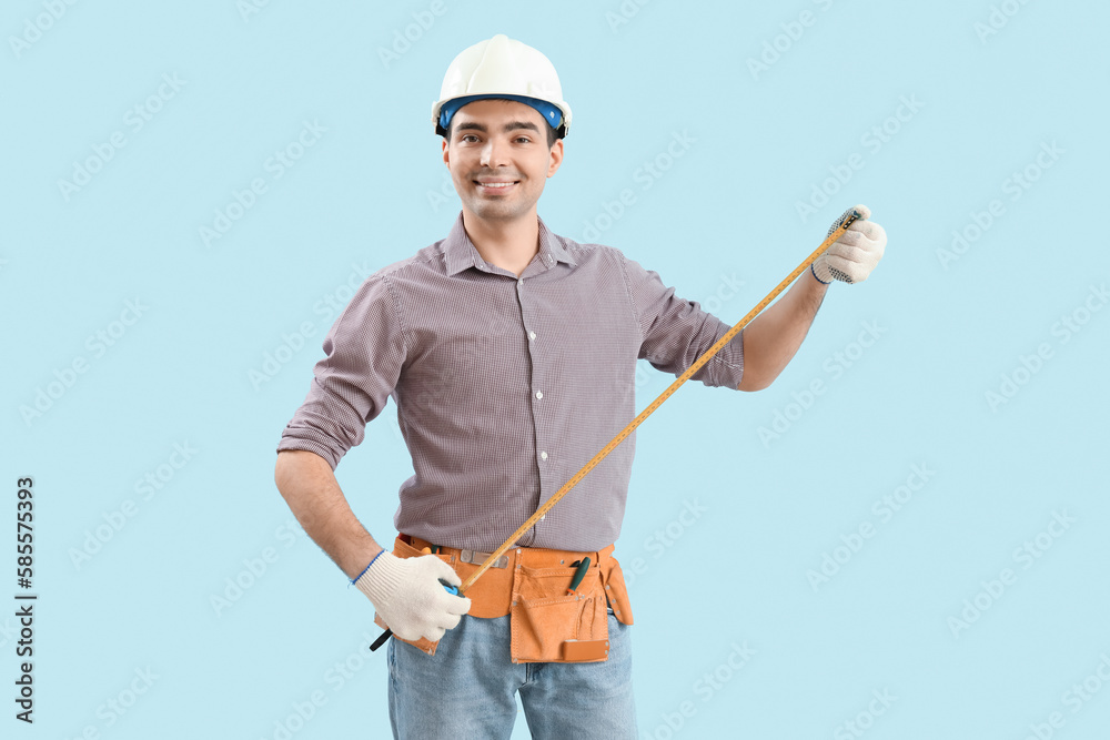 Young carpenter with tape measure on blue background