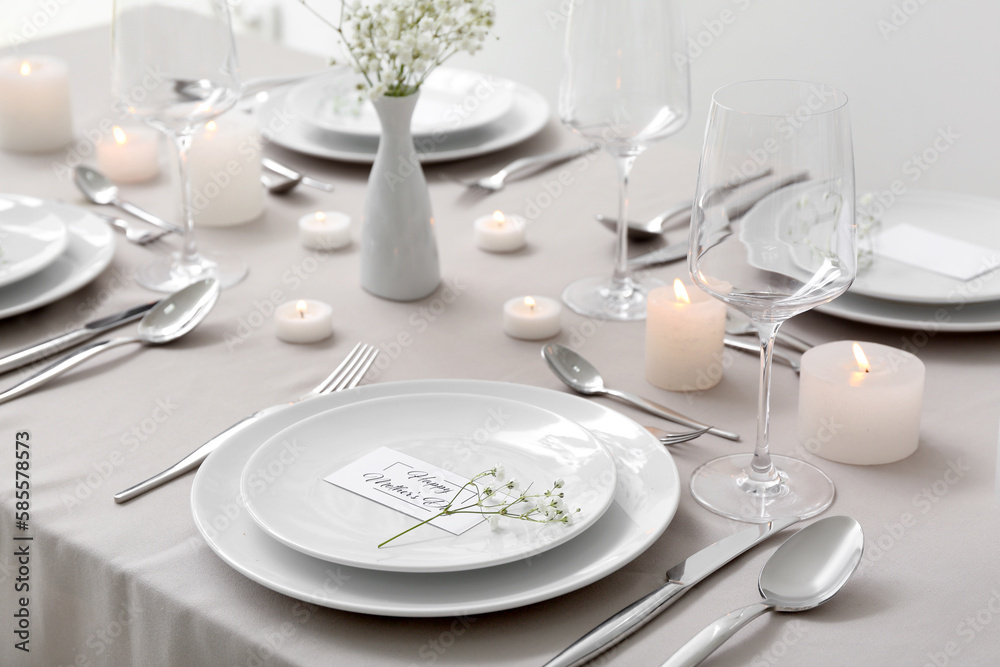 Setting for Mother's Day celebration with gypsophila flowers and burning candles on table Setting for Mother's Day celebration with gypsophila flowers and burning candles on table