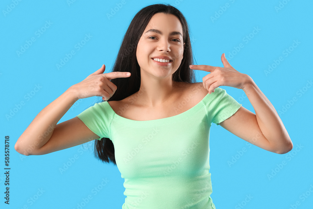 Fototapeta premium Beautiful young woman pointing at her smile on blue background