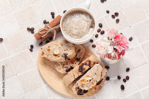 Board with delicious biscotti cookies, cup of coffee, flowers and beans on tile background