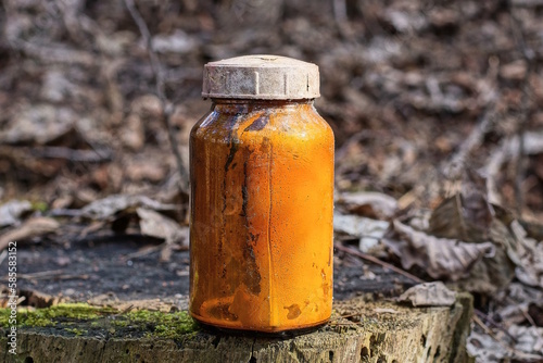 one old glass brown jar with yellow liquid stands on a gray stump outdoors in nature