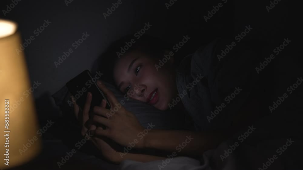 Young Asian woman using a smartphone in her bed at night. Young Asian woman using a smartphone in her bed at night.