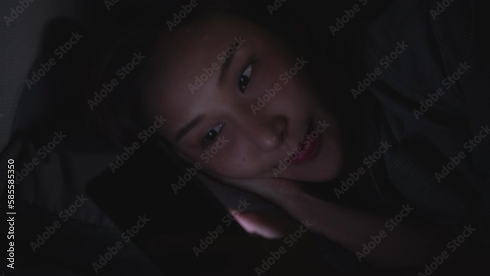 Young Asian woman using a smartphone in her bed at night. Young Asian woman using a smartphone in her bed at night.