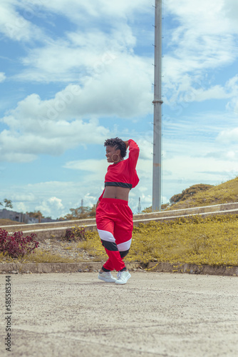 Jover mujer afro realiza baile estilo urban en parque local con hermoso y grande cielo y vegetacion.