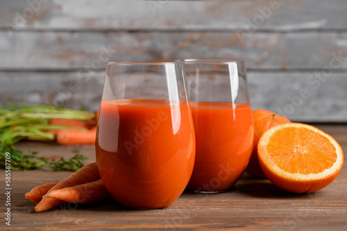 Two glasses of fresh carrot juice and orange on wooden table