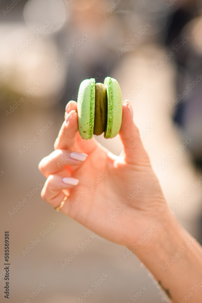close-up of female hand holding delicious bright green macaron on blurred background close-up of female hand holding delicious bright green macaron on blurred background