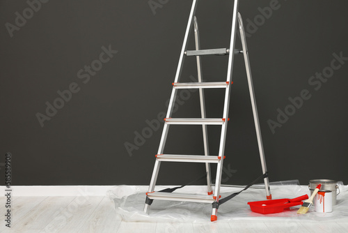 Metallic folding ladder and painting tools near gray wall indoors, space for text