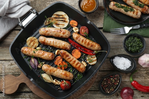 Tasty fresh grilled sausages served with vegetables on wooden table, flat lay