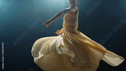 Graceful ballerina dances in light flowing dress on stage in pointlight in stage smoke. Ballet dancer performs dance elements of classical ballet