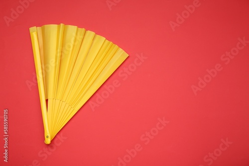 Bright yellow hand fan on red background  top view. Space for text