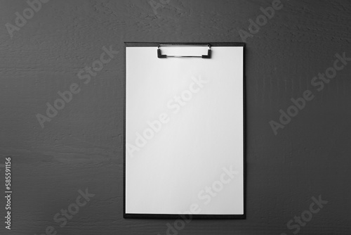 Clipboard with sheet of paper on black wooden table, top view. Space for text