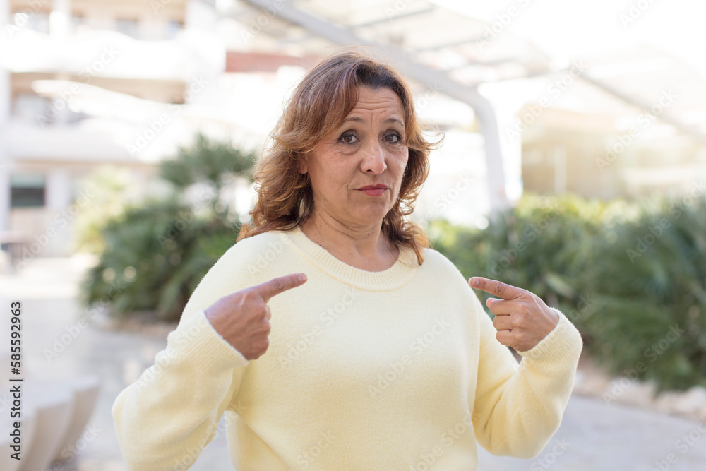 middle age woman with a bad attitude looking proud and aggressive, pointing upwards or making fun sign with hands