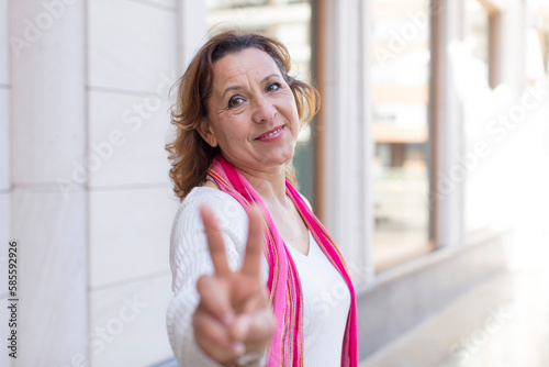 middle age woman smiling and looking happy, carefree and positive, gesturing victory or peace with one hand