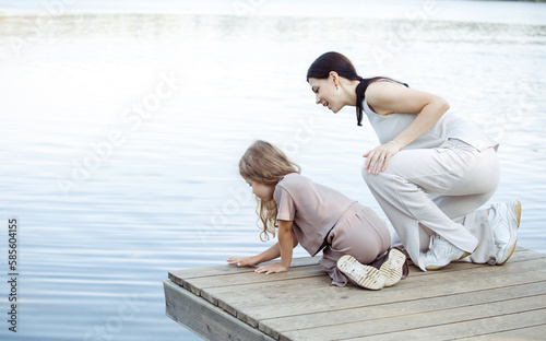 A young mother and her five-year-old daughter watch the fish in the lake, standing on the bridge.