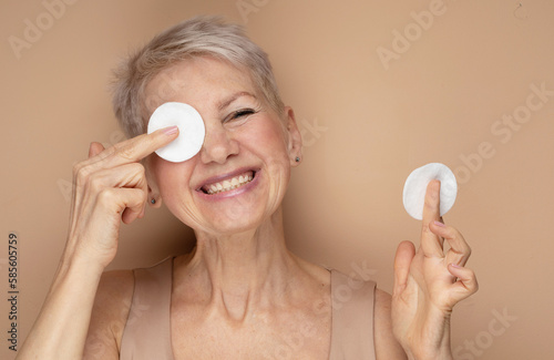 Beautiful elderly 60s woman with short hair doing her everyday routine removing her makeup with cotton pad