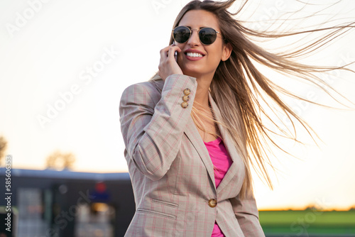 Beautiful young businesswoman using smartphone outdoors, hair flying on wind