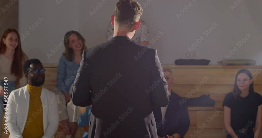 man handed microfoon to woman, lets her stand in front of audience, rear view, listeners warmly welcome the new lecturer in suit, in modern lecture hall or boardroom. view from back on speakers