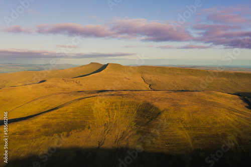 Expansive view of the Brecon Beacons at sunrise showcasing golden hills under a colorful sky in Wales photo