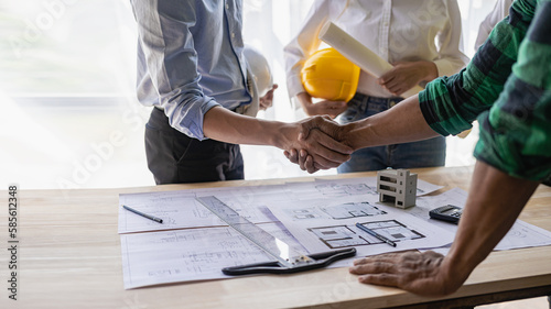 Yellow hard hat on table and house design print design with construction team handshake greeting start new project contract plan in office center at construction site partner and contractor photo