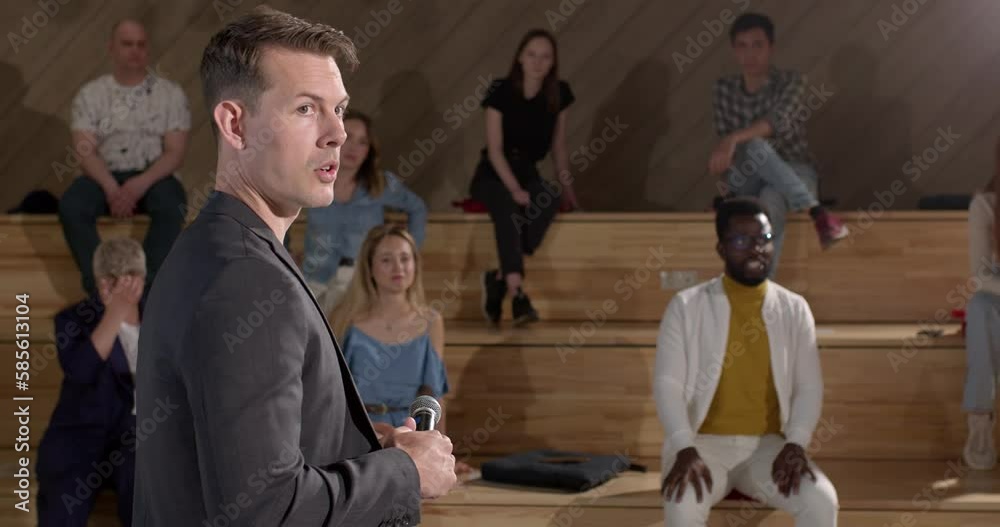 Confident speaker in suit giving a talk on corporate business meeting, using magnetic whiteboard and marker. Audience listening at conference hall. Business and Entrepreneurship event. Side View