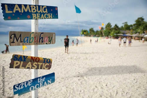 Dream beach of Moalboal Cebu in the Philippines with palm trees along the beach and a colorful wooden signpost sharp in the foreground.