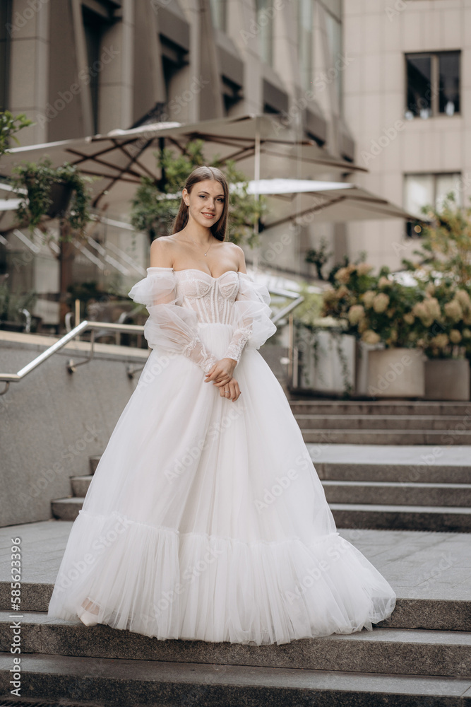 Fototapeta premium Full length portrait of beautiful bride in a white gorgeous wedding dress. Fashionable wedding dress with cleavage, wide long sleeves decorated with lace and beads