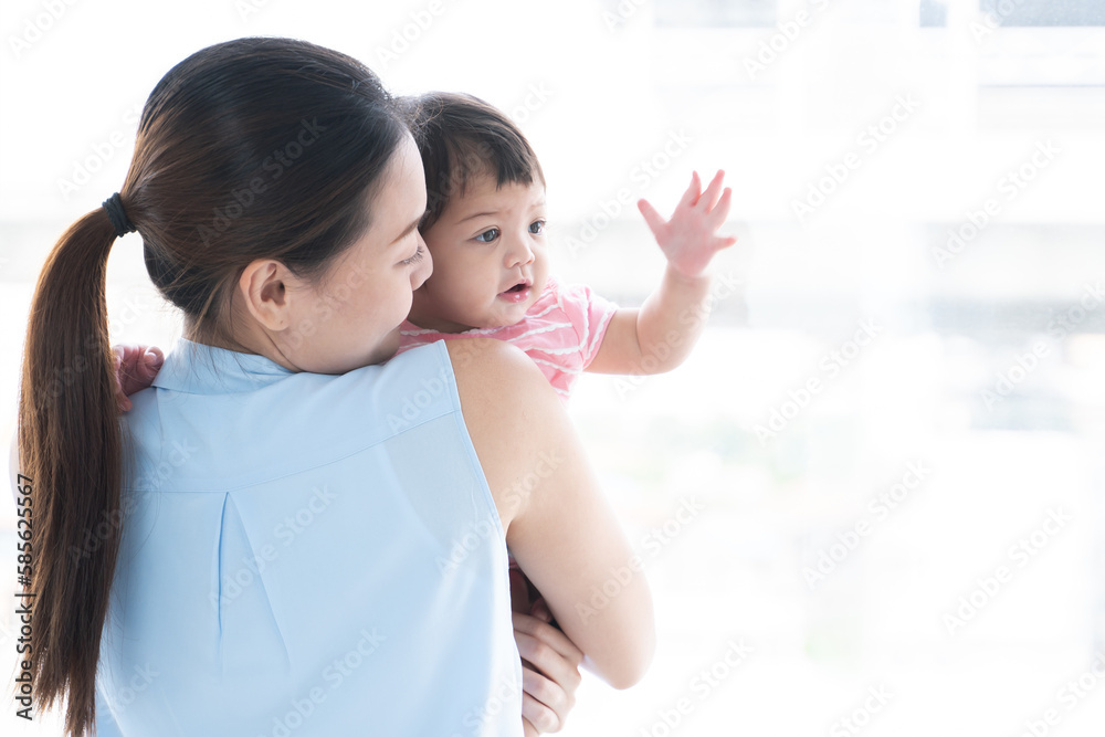 Young beautiful mother holding and looking at her cute little Caucasian 7 months newborn baby on her hands, standing near window at home. Happy family bonding, spending time together. Copy space Young beautiful mother holding and looking at her cute little Caucasian 7 months newborn baby on her hands, standing near window at home. Happy family bonding, spending time together. Copy space