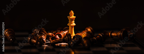 Photo Close-up leader chess piece standing with falling silver pawn chess pieces on chessboard on dark background