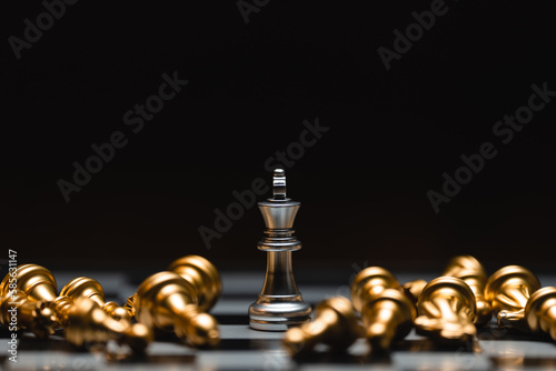 Close-up leader chess piece standing with falling silver pawn chess pieces on chessboard on dark background. Leadership and winner competition or business success teamwork strategy concept