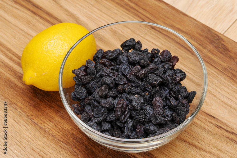 Blue raw raisins in a glass bowl on a wooden table, next to a lemon. Blue raw raisins in a glass bowl on a wooden table, next to a lemon.