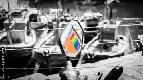 Colorful building reflection in a rearview mirror with boats and ships in black and white and out of focus in the background