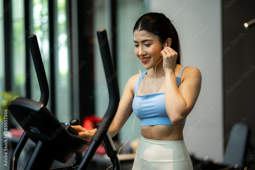 Young woman wearing earphones is choosing workout music with smart phone to listen while practicing in gym, Technology to stay fit and motivated Young woman wearing earphones is choosing workout music with smart phone to listen while practicing in gym, Technology to stay fit and motivated