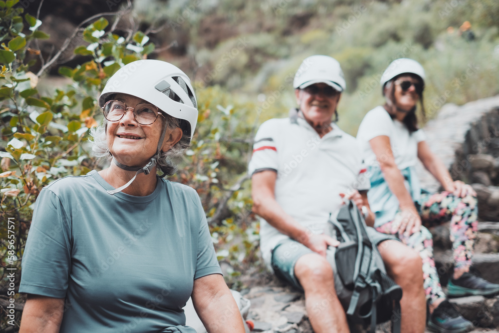 Group of smiling people in trekking day in nature, resting in mountain wearing protective helmets. Senior man and women enjoying healthy lifestyle