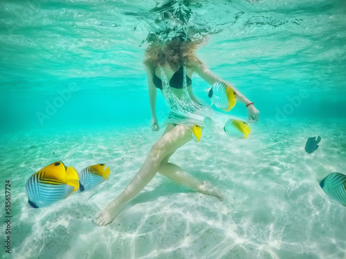 A beautiful girl among the inhabitants of the Indian Ocean. Undersea world. Coral fish. Fish swim around the girl's beautiful legs. Under the water. Beautiful sea. colorful ocean fish