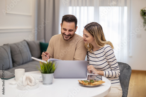 Married couple sit at a table in the living room with laptop working from home office