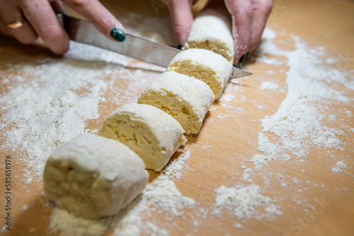 closeup of female hands in flour with a knife cut dough sausage in small pieces