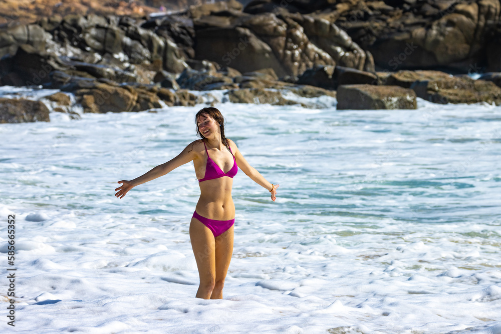 A beautiful girl in a pink bikini enjoys a sunny day and plays with the waves on an intimate second bay near Coolum beach, Sunshine coast, Queensland, Australia