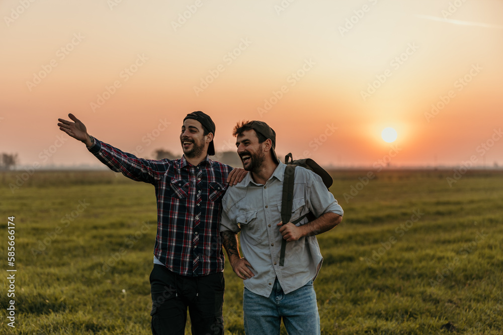 Two male friends walk and talk outdoors on the field during the sunset.