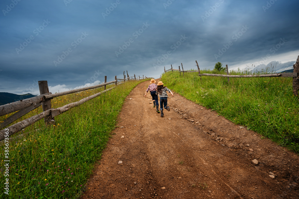 Two children run on road to the top of hill. Cloudy weather in mountains.