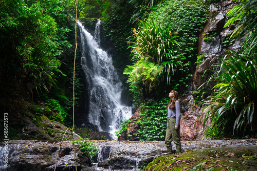 hiker girl stands gazing at an amazing tropical waterfall (elabana falls) in lamington national park near gold coast and brisbane in queensland, australia; rainforest waterfall amidst lush vegetation photo