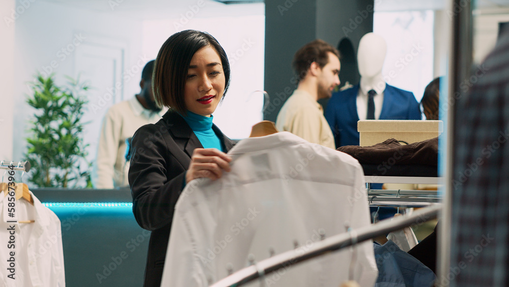 Asian customer looking at formal wear shirt in retail shop, using fashionable brands to increase wardrobe. Female adult buying fashion boutique merchandise, small business concept. Asian customer looking at formal wear shirt in retail shop, using fashionable brands to increase wardrobe. Female adult buying fashion boutique merchandise, small business concept.