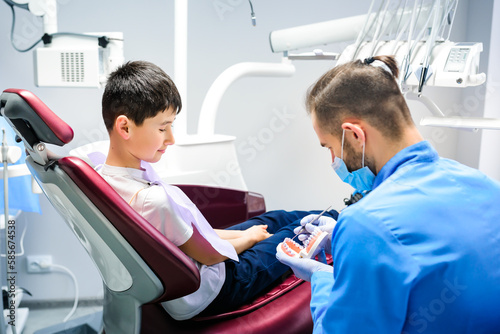 The dentist tells the boy about the prevention of dental diseases. The child is sitting in a dental chair in the clinic.