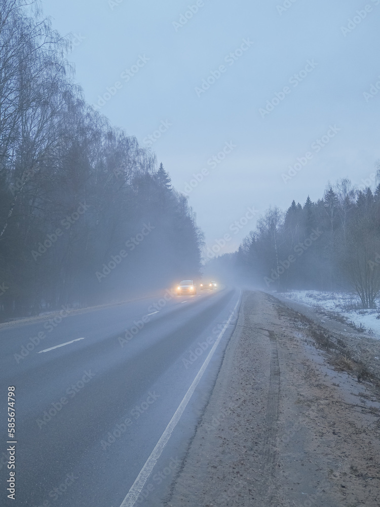 Obraz premium Blurred image of cars with headlights on driving on a country road in the fog.