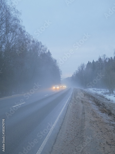 Blurred image of cars with headlights on driving on a country road in the fog.