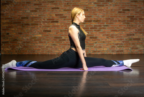 Young sporty attractive woman practicing yoga. working out, wearing sportswear, pants and top, indoor full length, yoga studio