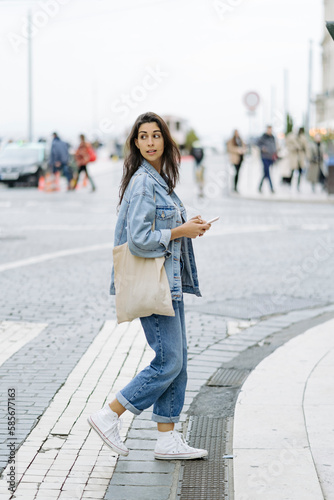 Young woman with tote bag and smart phone crossing road photo