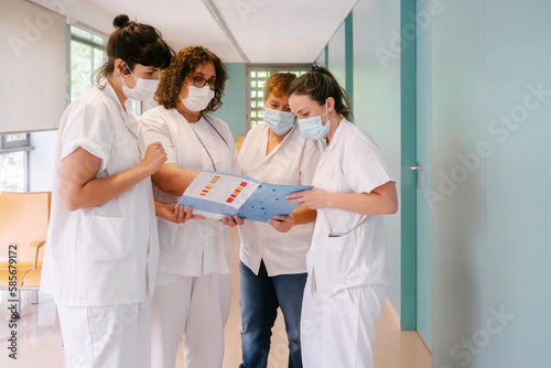 Doctor explaining medical report to colleagues standing at hospital corridor photo