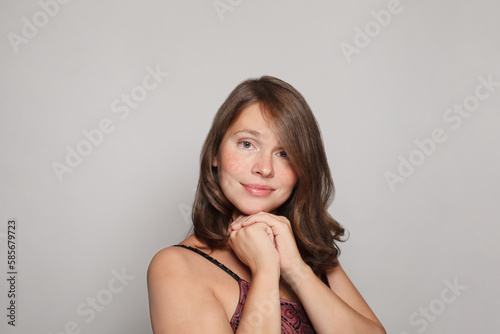 Close up studio shot of beautiful young brunette woman model with curly hair looking at camera with charming cute smile while posing against white studio wall background