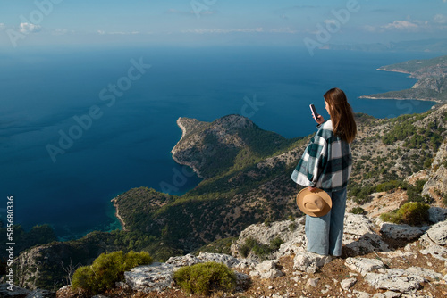 Woman photographing sea through smart phone standing on cliff
